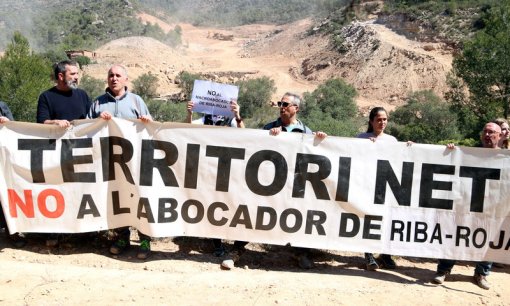 Pla general dels membres de les plataformes 'Almatret Net' i la 'Ribera Digna' en l'acció per denunciar el projecte de l'abocador de residus de Riba-roja i al fons les màquines que treballen en els terrenys. Imatge del 13 d'abril del 2019 (Horitzontal).